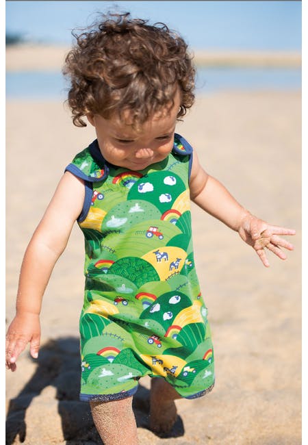 Baby am Strand mit grüner Sommerstrampler / Traktor von der Marke Frugi